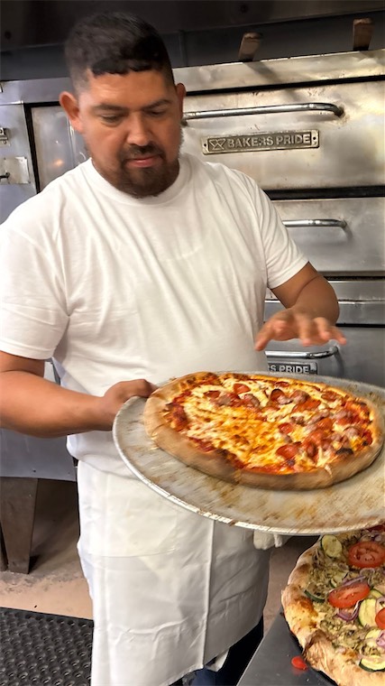 DeVino's pizza maker holding fresh pizzas from the oven